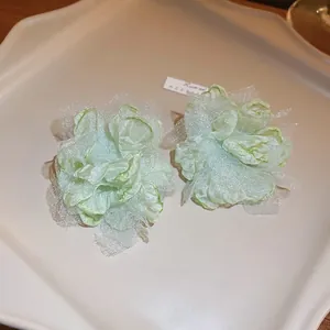 Detailed close-up of light green mesh flower earrings on a cream ceramic plate