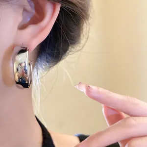 Close-up of silver-toned thick hoop earring on ear with high-polish mirror finish.