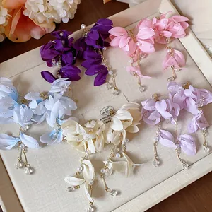 Eleganti orecchini multicolori a fiore in tessuto con lunghe nappe di perle su un vassoio.
