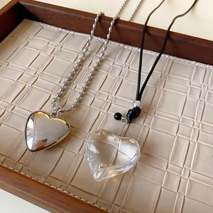 Close-up of metallic silver and clear glass heart pendant necklaces on a wooden tray.