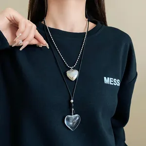 Model wearing a long black cord necklace with a transparent heart pendant and silver chain.