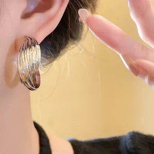 Detailed macro view of a silver-toned twisted metal hoop earring worn by a model.