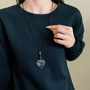 Detailed view of a minimalist transparent heart pendant necklace on a black sweater.