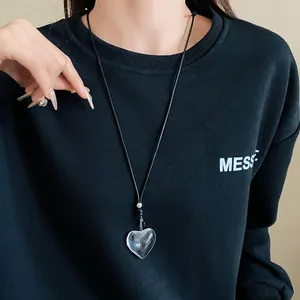 Detail shot of a transparent heart pendant necklace worn on a black sweatshirt