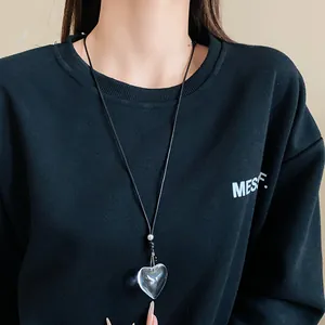 Close-up of a minimalist transparent heart pendant necklace on a black sweater
