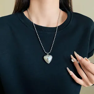 Close-up of a silver heart pendant necklace with a delicate rice bead chain on a black sweater.