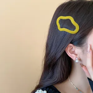 Close-up view of yellow flocked irregular hair clip worn on side of model's dark hair