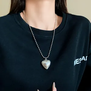 Macro view of a stylish silver heart pendant necklace worn on a black sweatshirt