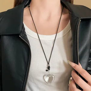 Close-up detail of clear heart pendant necklace worn over white top and black jacket