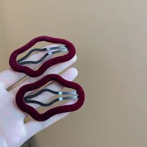 Detail view of two burgundy flocked irregular geometric BB hair clips held in hand