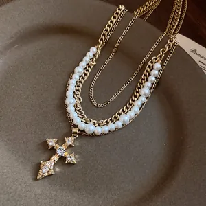 Detailed view of an ornate gold rhinestone cross pendant on a multi-layer pearl necklace