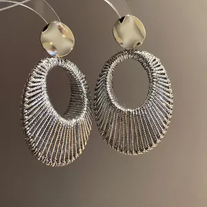 Macro dettagli di orecchini pendenti ovali argentati con design intrecciato complesso