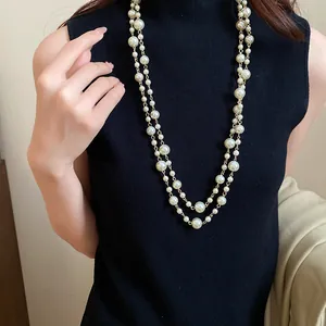 Close-up detail of elegant multi-layer long pearl necklace styled on a black knitted top.