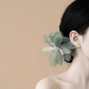Close-up detail showing the delicate green fabric flower hair pin with a dangling pearl tassel