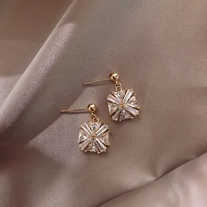 Exquisite close-up of geometric zircon stud earrings resting on elegant champagne silk fabric