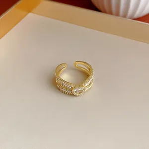 Primo piano di un anello aperto dorato con zircone a cuore e raffinate perle piccole.