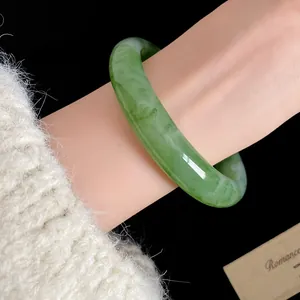 Dettaglio di un bracciale in resina marmorizzata verde al polso con maglione bianco.