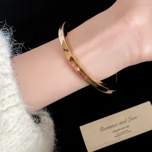 Elegante bracciale rigido dorato minimalista con finitura lucida indossato al polso