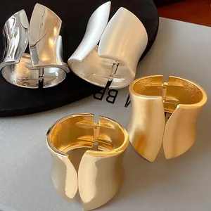 Set of wide asymmetrical matte and polished metal cuff bracelets in gold and silver tones.