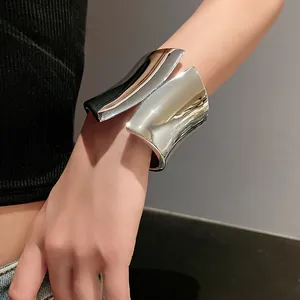 Detailed view of a wide asymmetric shiny silver open cuff bracelet worn on a wrist
