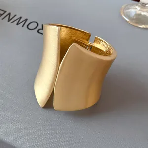 Detailed macro view of wide asymmetric gold cuff bracelet with brushed matte finish