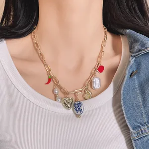 Detailed view of a gold-toned necklace with chili, pearl, and heart charms on a model.