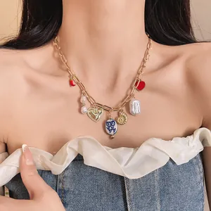 Close-up of gold chain necklace with heart, pearl, and chili charms on a female model