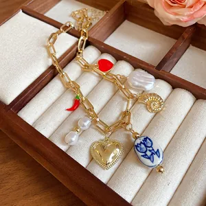 Detailed view of gold link chain necklace featuring heart, chili, pearl, and floral ceramic charms