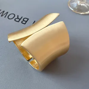 Macro detail of a golden asymmetric wide cuff bracelet with a matte brushed finish