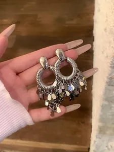 Nahaufnahme von silbernen runden Ohrringen mit Metallpaillettenfransen an der Hand.