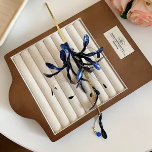 Elegant vintage blue floral hairpin with long golden tassel on cream jewelry display tray