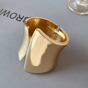 Detailed macro view of a wide gold asymmetrical open bangle with a smooth reflective finish
