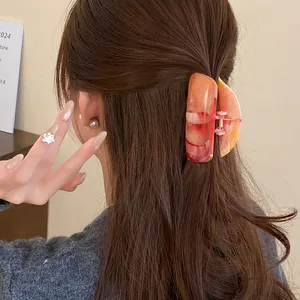 Close-up view of an orange marble-patterned acrylic hair claw clip worn on brown hair