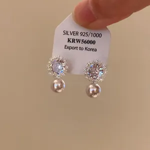 Dettaglio macro di eleganti orecchini a lobo a fiore con zirconi e pendenti in perla bianca