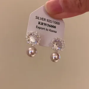 Dettaglio di eleganti orecchini a lobo a fiore in argento e zirconi con perle