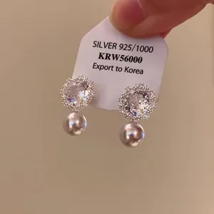 Dettaglio di orecchini a lobo con fiori in zircone e eleganti perle su cartoncino.