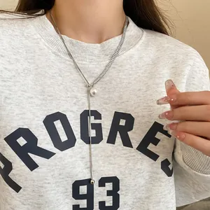 Close-up of long Y-shaped necklace with pearl and zircon pendant on a grey sweatshirt.