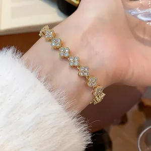 Close-up of gold-plated clover bracelet with sparkling cubic zirconia on a wrist.