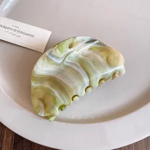 Close-up detail of a minimalist marble green acrylic hair claw clip on a white ceramic plate