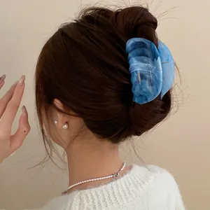 Close-up of a stylish blue marbled acrylic hair claw clip on a model's brunette bun