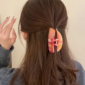 Detailed view of an elegant orange marble acrylic hair claw clip styled on brunette hair.