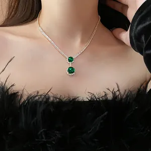 Close-up detail showing an elegant emerald green gemstone necklace worn with a black feather top