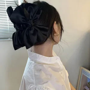 Dettaglio posteriore di una grande clip a fiocco in raso nero indossata da una modella.