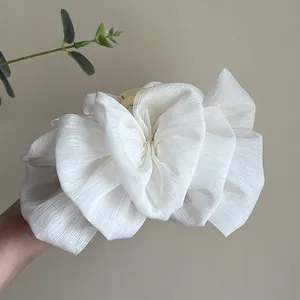 Detailed view of an elegant white pleated fabric flower hair claw clip for bun styling.