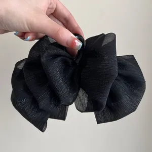 Close-up of black oversized fabric bow hair claw clip with shimmering pleated texture