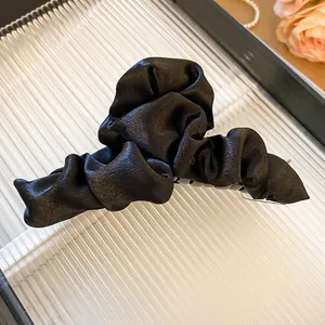 Detailed view of elegant black ruched fabric hair claw clip with smooth silk texture finish