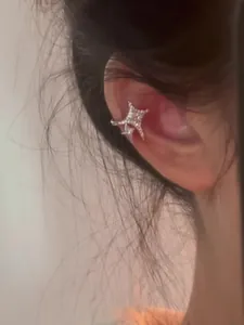 Close-up view of a delicate sparkling star-shaped zircon ear cuff on a female model's ear