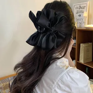 Dettaglio di una grande molletta per capelli a fiocco in raso nero su capelli lunghi.