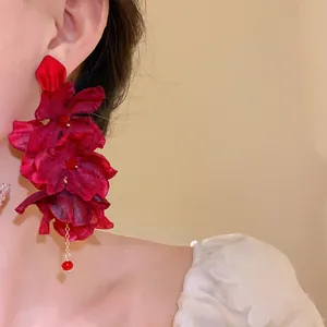 Detailed view of handmade red fabric flower earrings with elegant bead tassels on ear