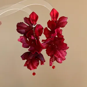 Detail view showing elegant red fabric flower earrings with gold chain tassels and beads